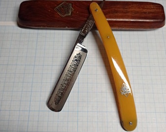May include: A yellow and silver straight razor with the words "Puma Solingen" engraved on the blade. The razor is in a wooden case.