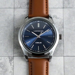 May include: A silver watch with a blue face and brown leather band. The watch face has the words "Langdon" and "Jubilee" printed on it.
