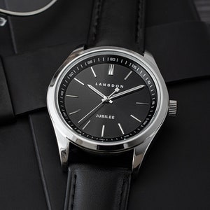 May include: A silver watch with a black leather band and a black face. The watch face has white markings and the words "Langdon" and "Jubilee" printed on it.