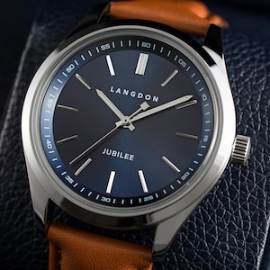 May include: A silver watch with a blue face and a brown leather band. The watch face has white markings and the words "LANGDON" and "JUBILEE" printed on it.