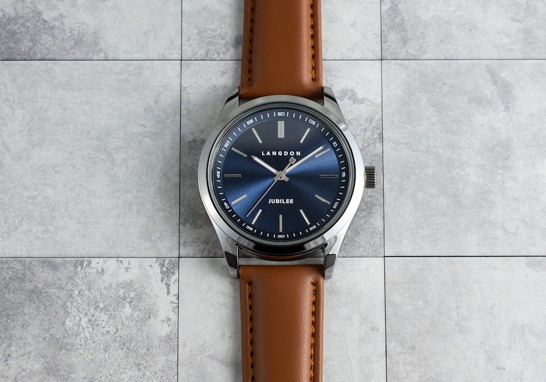 May include: A silver watch with a blue face and brown leather band. The watch face has the words "Langdon" and "Jubilee" printed on it.