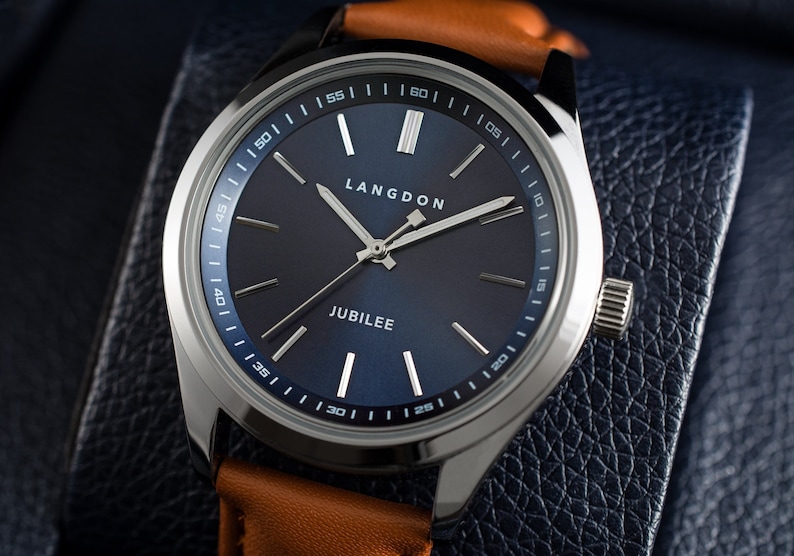 May include: A silver watch with a blue face and a brown leather band. The watch face has white markings and the words "LANGDON" and "JUBILEE" printed on it.