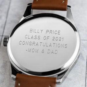 May include: A silver watch with a brown leather band. The back of the watch is engraved with the text "Billy Price Class of 2021 Congratulations -Mom & Dad".