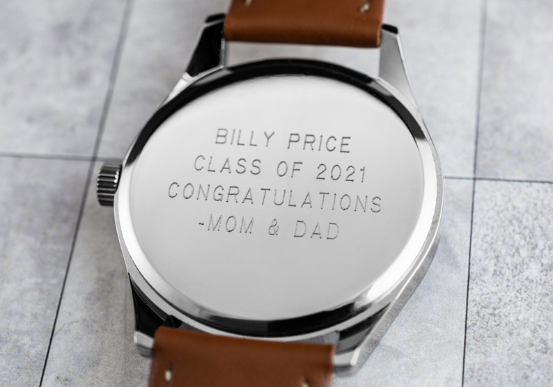 May include: A silver watch with a brown leather band. The back of the watch is engraved with the text "Billy Price Class of 2021 Congratulations -Mom & Dad".