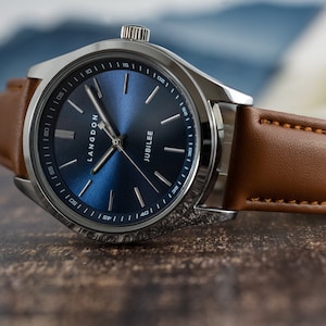 May include: A silver watch with a blue face and brown leather band. The watch face has the words "Langdon Jubilee" printed on it.