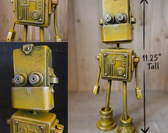 May include: A yellow robot figurine with a rectangular head, two circular screw-like eyes, and a square torso featuring mechanical details. The robot stands on two legs with circular feet and measures 11.25 inches tall as indicated by the text.