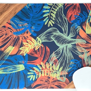 Peut inclure: Un tapis de souris avec un fond bleu foncé et un motif de feuilles tropicales colorées. Les feuilles sont dessinées dans un style stylisé, dessiné à la main et sont dans des tons de bleu, vert, jaune, orange et rouge.