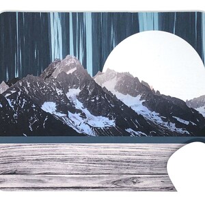Peut inclure: Un tapis de souris avec un collage numérique d'une chaîne de montagnes avec un grand cercle blanc dans le ciel et un fond en bois.