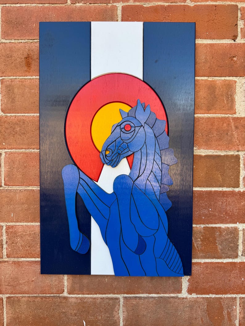 Puede incluir: Arte mural de madera con la bandera del estado de Colorado y un caballo azul. La obra de arte tiene un fondo azul marino con una franja blanca y un c&iacute;rculo rojo y amarillo. El caballo es azul con ojos rojos.