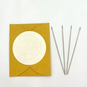 May include: A set of five silver needles packaged in a brown paper envelope with a white circle sticker featuring a geometric design.
