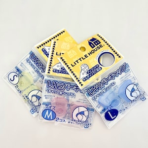 Pode incluir: Três pacotes de dedal de borracha da marca Little House em tamanhos diferentes: pequeno, médio e grande. Cada pacote tem um design amarelo e azul com o nome da marca e uma imagem de uma casa. Os dedales são transparentes e vêm em diferentes cores: amarelo, rosa e azul.