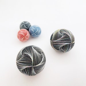 May include: Four decorative balls, two black and white, one red and white, and one blue and white. The balls are made of a soft, textured material and have intricate patterns.
