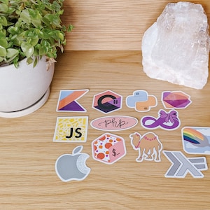 Könnte beinhalten: Eine Sammlung bunter Aufkleber mit verschiedenen Logos von Programmiersprachen, darunter JavaScript, PHP, Python, C# und Kotlin. Es gibt auch Aufkleber mit einem Regenbogen, einem Kamel und einem Unendlichkeitszeichen.
