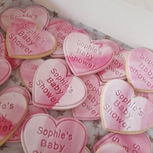 May include: A close-up of pink and white heart-shaped cookies decorated with the text "Sophie's Baby Shower".