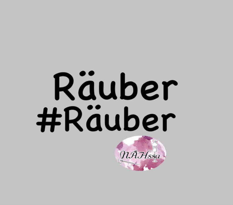 May include: Black text on a grey background reads "R&auml;uber #R&auml;uber". A pink and white watercolour oval with the text "N&Auml;Hssa" is in the bottom right corner.
