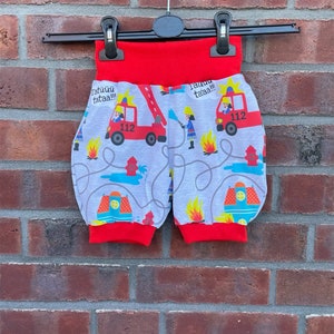 Könnte beinhalten: Rote und graue Kinderhose mit Feuerwehrwagen-Muster. Die Hose hat roten Gummizug an der Taille und an den Beinen. Die Feuerwehrwagen haben die Nummer 112 und den Text "Tatüüü tataa!!" drauf.