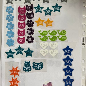 Könnte beinhalten: Eine Sammlung bunter Aufkleber mit Zahlen darauf. Die Aufkleber haben die Form von Sternen, Herzen, Blumen, Tieren und Walen. Die Zahlen auf den Aufklebern reichen von 50 bis 116.