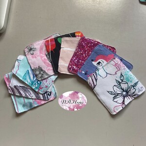 Könnte beinhalten: Ein Set aus acht bunten Stoffquadraten mit verschiedenen Mustern, darunter Blumen-, geometrische und Tiermotive. Die Quadrate sind in einer Halbkreisform angeordnet, wobei der Text "N.A.Hssa" in der unteren Mitte des Bildes sichtbar ist.