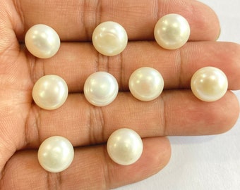 May include: Ten white round pearls, each with a smooth, glossy surface, are displayed on a hand.