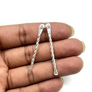 Könnte beinhalten: Ein Paar silberfarbene, gedrehte Metall-Schmuck-Findings.