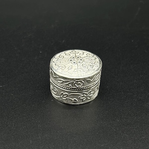 May include: A silver trinket box with an intricate floral design. The box is round and has a lid.