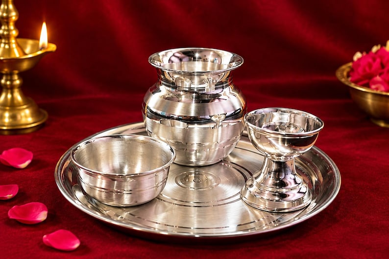 May include: A polished silver-toned metal set consisting of a round tray, a small bowl, a rounded pot with a flared rim, and a pedestal-style cup. The items feature smooth, reflective surfaces with subtle horizontal etched lines for decoration.