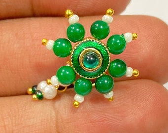 May include: A green and gold flower-shaped nose ring with a green gem in the center. The ring is made of beads and wire.