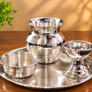 May include: A polished silver-toned metal set consisting of a round tray, a small bowl, a wide-mouthed pot with a rounded body, and a pedestal-based cup. Each piece features a smooth, reflective surface with subtle horizontal grooved detailing.