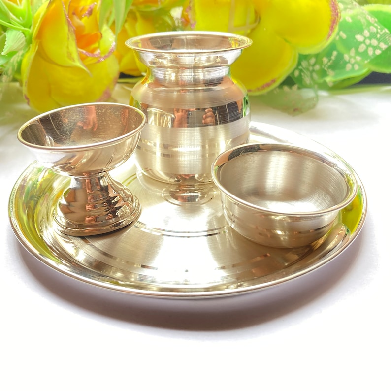 May include: A polished silver-toned metal set consisting of a round tray, a small pedestal bowl, a wider bowl, and a central pot. The items feature a smooth, reflective finish with subtle horizontal line detailing on the pot and tray surface.
