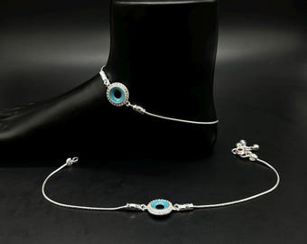 May include: A silver anklet featuring a turquoise blue central stone encircled by clear crystals. The anklet is shown on a black foot form, with a second anklet below. The jewellery has a delicate, elegant design.