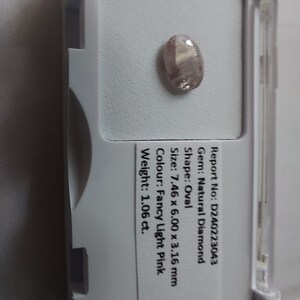 May include: A light pink oval-shaped diamond gemstone in a white plastic display case. The diamond is 7.46 x 6.00 x 3.16 mm and weighs 1.06 carats. Report No: D240223043.