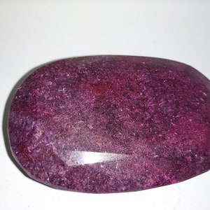 Może przedstawiać: Duży, owalny, fioletowy kamień szlachetny o szlifie fasetowym. Kamień szlachetny ma lekko zamglony wygląd z nutą blasku.