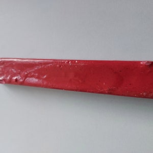 May include: A red sealing wax stick, used for sealing envelopes and letters.