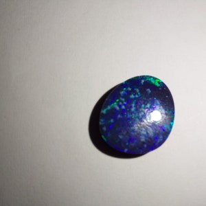 May include: A dark blue oval opal gemstone with green and white flashes of color.