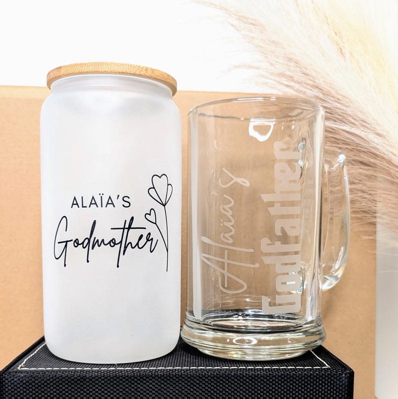 Pu&ograve; includere: Un barattolo di vetro smerigliato con un coperchio in bamb&ugrave; e una tazza di vetro. Il barattolo ha il testo "Ala&iuml;a's Godmother" e un piccolo disegno di un fiore. La tazza ha il testo "Ala&iuml;a's Godfather" inciso su di essa.