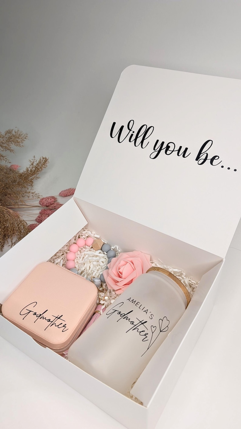 Pu&ograve; includere: Una scatola regalo bianca contenente un braccialetto in silicone rosa e grigio, una rosa rosa, una scatola per gioielli rosa con la scritta "Madrina" e un barattolo di vetro smerigliato con la scritta "Madrina di Amelia".