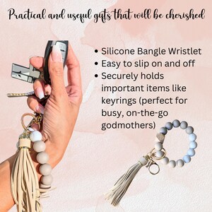 Pu&ograve; includere: Un braccialetto in silicone con un portachiavi a nappa beige. Il braccialetto &egrave; realizzato con perline grigie e bianche ed &egrave; progettato per contenere chiavi o altri piccoli oggetti. Il testo "Silicone Bangle Wristlet" &egrave; visibile nell'immagine.