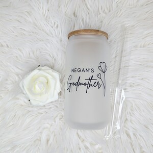 Pu&ograve; includere: Un barattolo di vetro bianco smerigliato con un coperchio in bamb&ugrave; e una scritta nera che recita "Negan's Godmother" con un semplice disegno di un fiore. Il barattolo &egrave; su una superficie bianca e soffice.