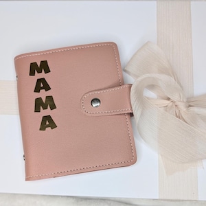 May include: A blush pink leather-bound journal with a gold foil inscription that reads "MAMA". The journal is wrapped in a white box with a cream-colored ribbon.