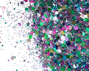 May include: A close-up of a pile of iridescent green, purple, and pink glitter. The glitter is scattered on a white background. The text "the GLITTER SHOPPE BY ORIGINAL SIX DESIGNS" is visible in the upper left corner of the image.