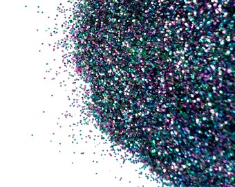 May include: A close-up of teal, purple, and black glitter. The glitter is scattered on a white background. The text "the GLITTER SHOPPE BY ORIGINAL SIX DESIGNS" is visible in the top center of the image.