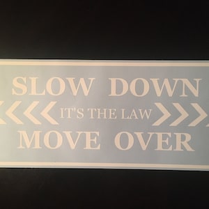 Puede incluir: Un letrero azul y blanco con el texto "Slow Down It's the Law Move Over" y flechas blancas apuntando hacia la izquierda y la derecha.