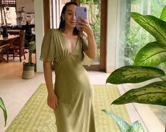 May include: Olive green dress with a V-neckline and short, flutter sleeves. The dress has a fitted bodice and a flowing skirt. The fabric appears to be a lightweight material. The dress is knee-length.