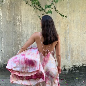 Puede incluir: Una persona lleva un vestido largo de color rosa y blanco con estampado tie-dye, espalda baja y tirantes finos. El vestido est&aacute; hecho de un material sedoso y tiene una silueta fluida.