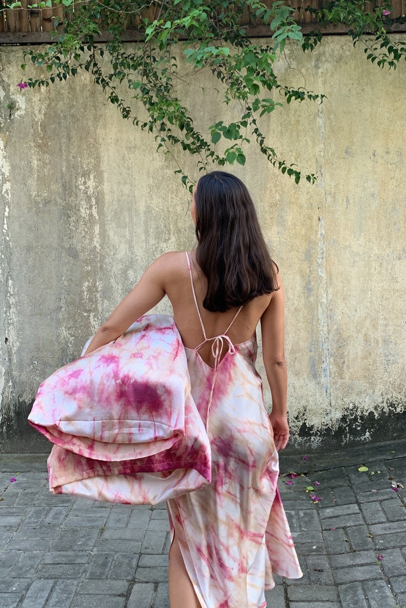 Puede incluir: Una persona lleva un vestido largo de color rosa y blanco con estampado tie-dye, espalda baja y tirantes finos. El vestido est&aacute; hecho de un material sedoso y tiene una silueta fluida.