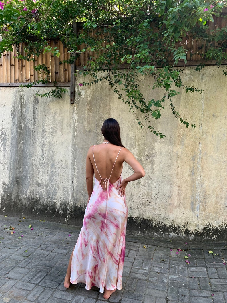 Puede incluir: Un vestido largo y fluido con un estampado tie-dye en tonos rosa, blanco y naranja. El vestido tiene la espalda baja y una abertura lateral.