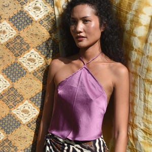 Könnte beinhalten: Ein fliederfarbenes Neckholder-Top aus seidigem Material. Das Top wird mit einem Rock mit einem schwarz-weiß-braunen Animal-Print kombiniert. Der Hintergrund umfasst gemusterte Stoffe in Gold- und Brauntönen.