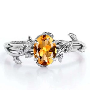 May include: A silver ring featuring a large oval topaz gemstone set in a delicate vine design. The ring has intricate details of leaves and branches.