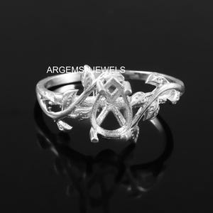 May include: Silver ring with a delicate floral design. The ring has a large oval-shaped setting in the center, perfect for a gemstone.