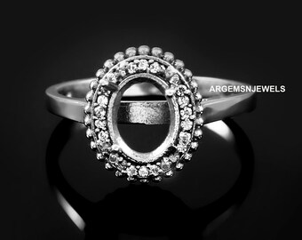 May include: A silver ring with an oval-shaped setting surrounded by a halo of small diamonds. The ring is designed to hold a larger gemstone in the center.